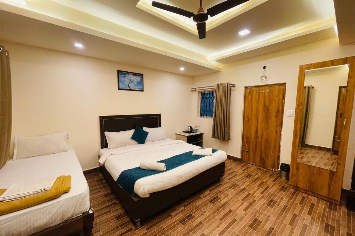 A hotel room with a large bed, a smaller bed, a ceiling fan, a nightstand, a mirror, and a wooden door.