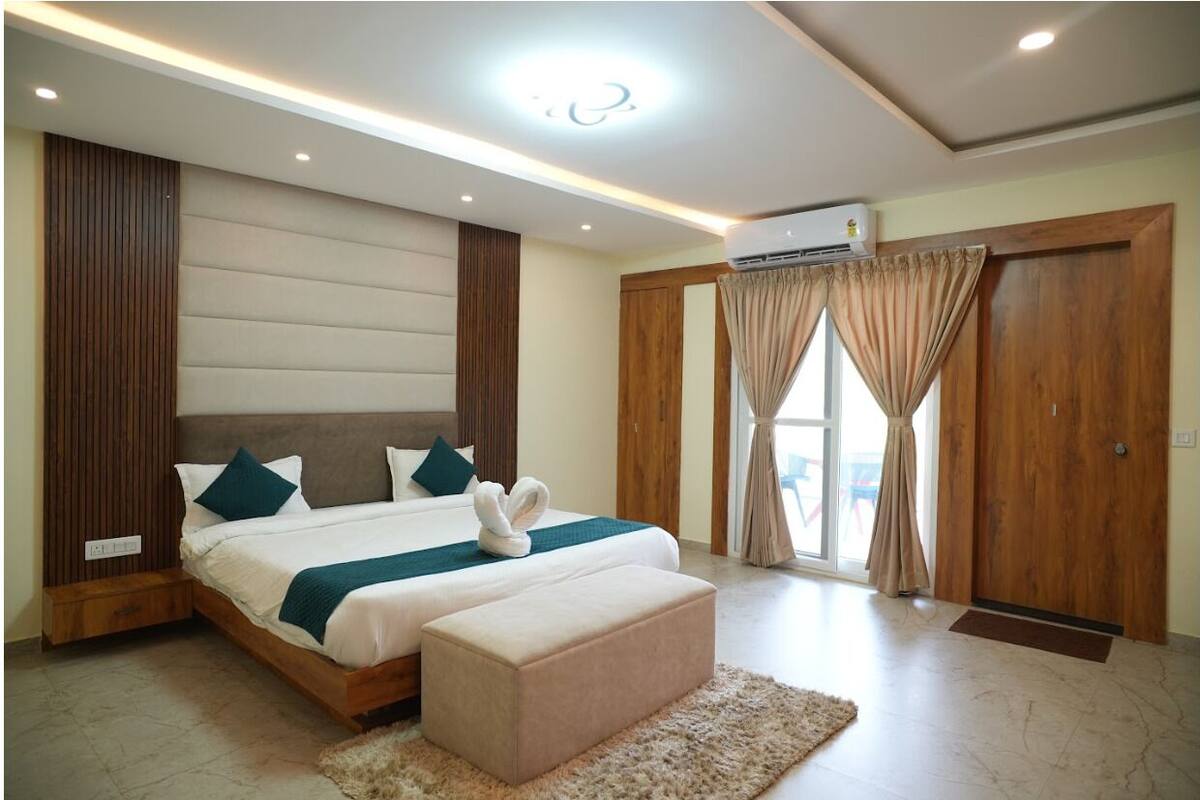 A modern bedroom with a large bed, a wooden headboard, a bedside table, and a window with curtains.