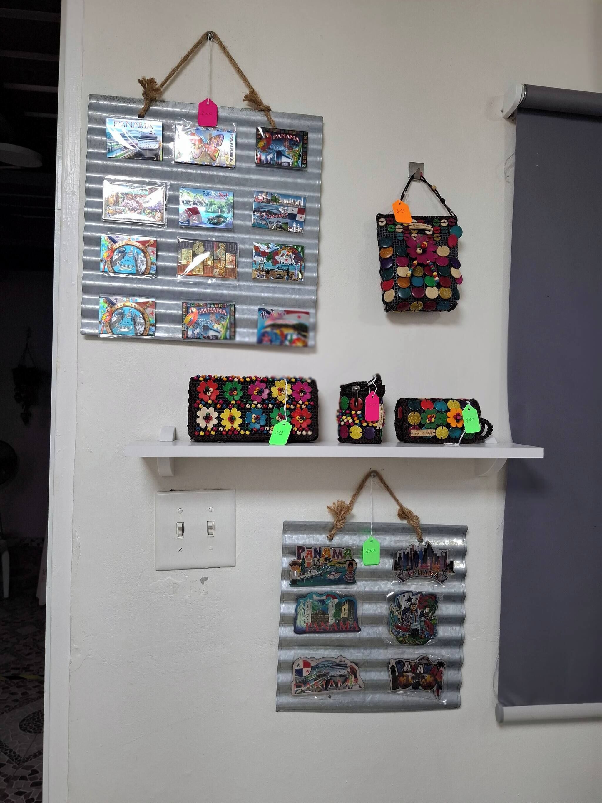 Una pared con varios elementos con temática de Panamá, incluyendo un panel metálico con postales, un bolso colorido y un estante con adornos.