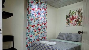 A bedroom with a bed, a chair, and a floral curtain. - Apartamento Lilia Airport 1 (Panamá)
