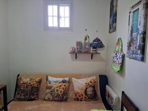 Ein Zimmer mit einer Couch, Kissen, einem Fenster, einem Regal mit Taschen und Wandbildern.