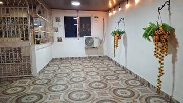 A room with patterned floor tiles, a window with curtains, a wall-mounted air conditioner, and hanging plants.