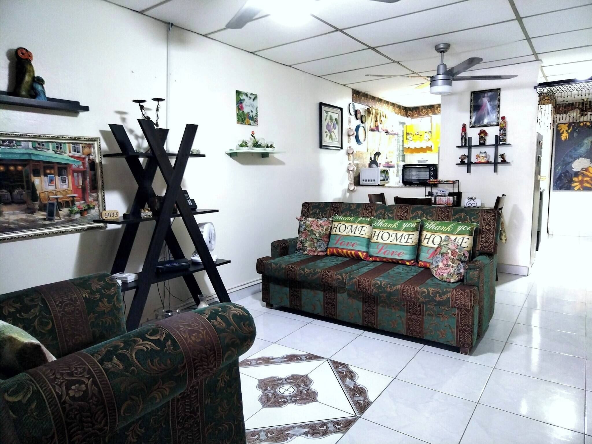 A living room with a sofa, a television, a ceiling fan, and various wall decorations.