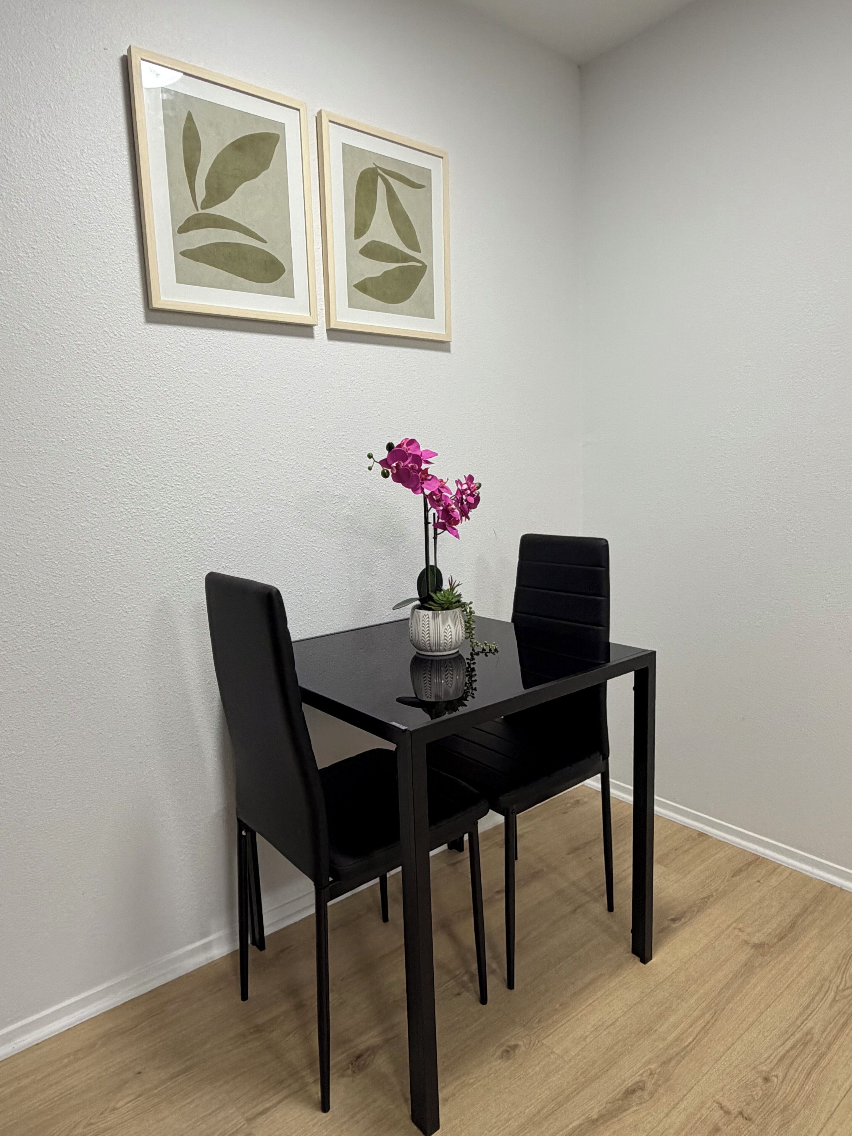 A dining table with chairs, a vase with flowers, and two framed pictures on the wall.