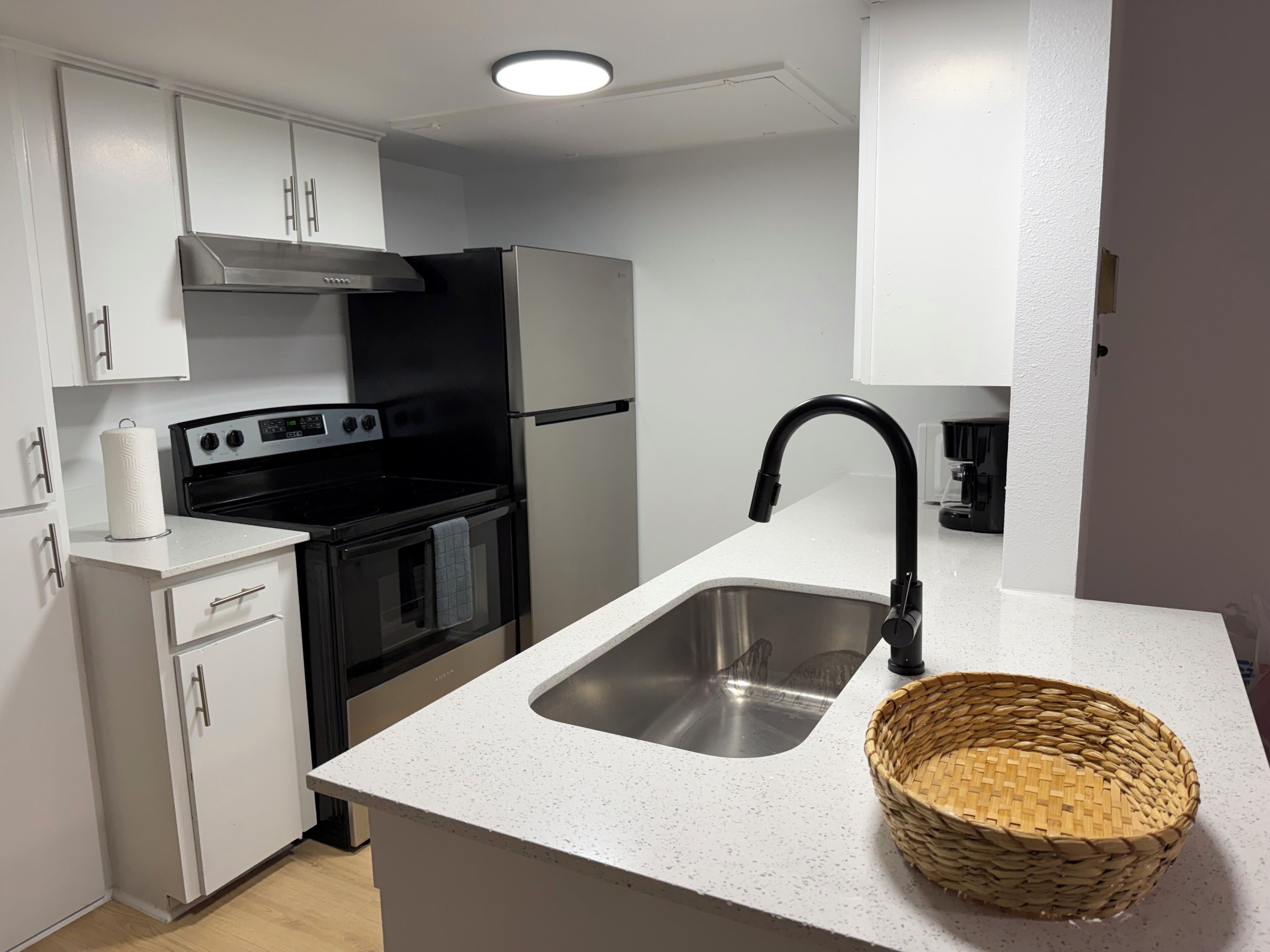 A modern kitchen with white cabinetry, a stainless steel sink, a black faucet, a stove, and a built-in oven.
