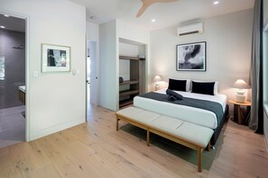Een moderne slaapkamer met een bed, nachtlampen, een bankje, een inloopkast en een badkamer.