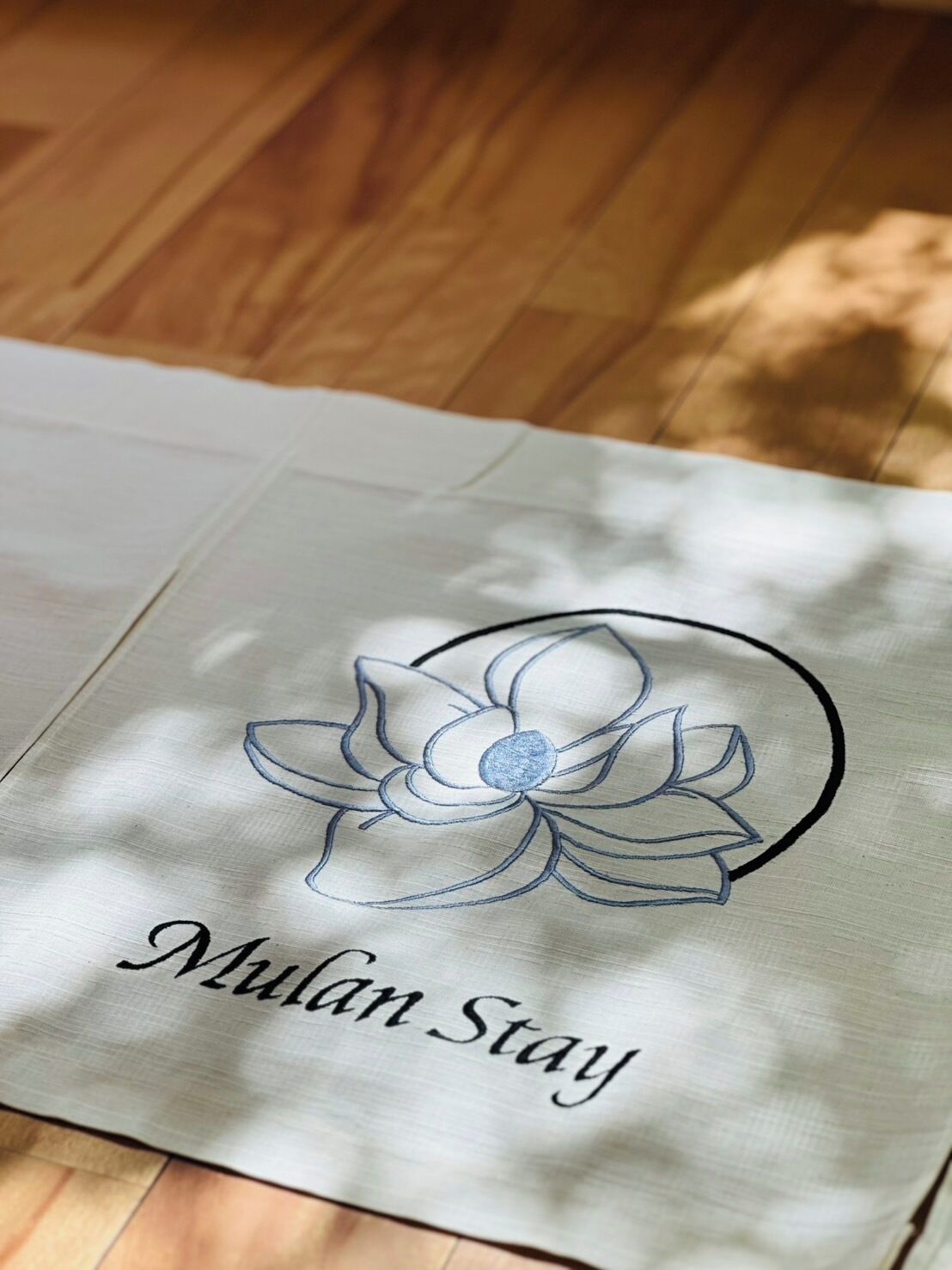 A white tote bag with a floral design and the text 'Mulan Stay' embroidered on it.