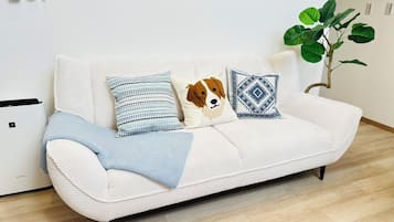 A white sofa with patterned pillows, a blue throw blanket, and a plant in a corner.