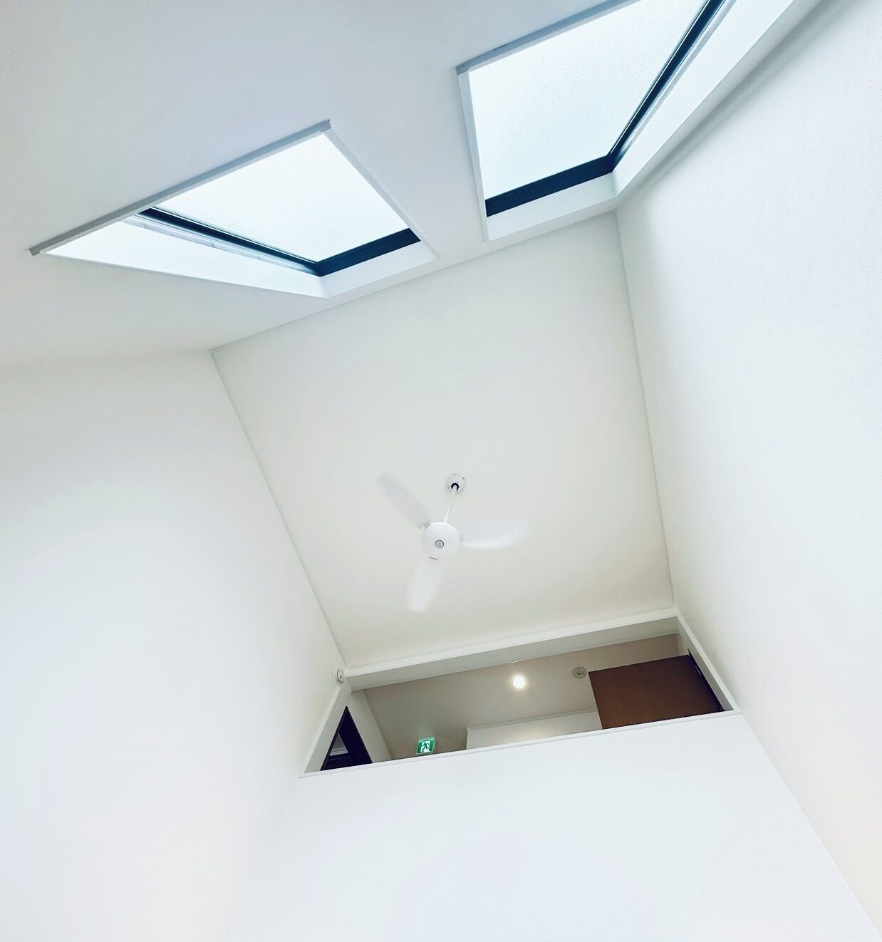 A room with a skylight, a ceiling fan, and a visible door leading to another room.