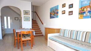 Ein Wohnzimmer mit Sofa, einem Esstisch mit Stühlen, einer Treppe und Wandbildern.