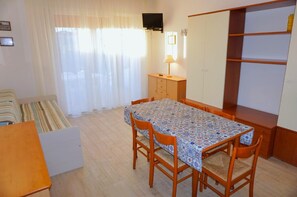 Quarto compacto com mesa de jantar, cadeiras, sofá, televisão fixada na parede e guarda-roupa.