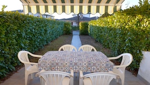 Eine überdachte Terrasse im Freien mit Tisch und Stühlen, umgeben von Hecken.