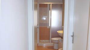 Ein schmales Badezimmer mit Dusche, Toilette und Waschbecken.
