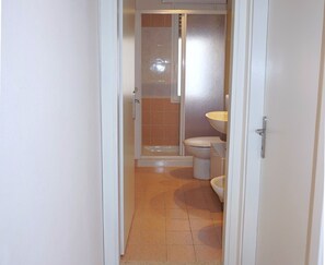 Ein schmales Badezimmer mit Dusche, Toilette und Waschbecken.