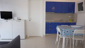 A compact kitchen with blue cabinets, a dining table with chairs, a TV on a cabinet, and a door. - Apartment in Caorle Near Sandy Beaches (Caorle)
