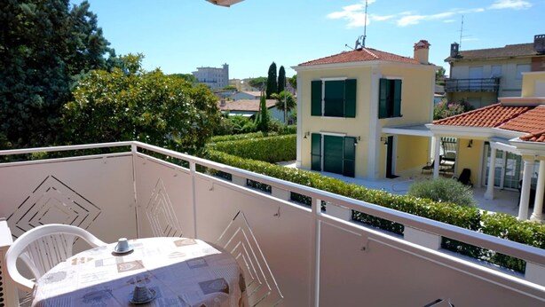 A balcony with a table and chairs, a view of a yellow building, and a well-maintained garden. - Apartment in Caorle Near Sandy Beaches (Caorle)