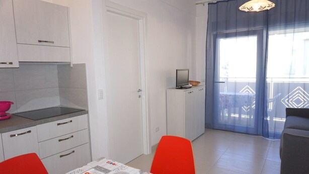 Een knus woongedeelte met een kitchenette, een eethoek met tafel en stoelen, een televisie op een kast, en een balkon met uitzicht.