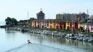 A waterfront area with colorful buildings, a marina with boats, and a person on a jet ski. - Apartment in Caorle Near Sandy Beaches (Caorle)