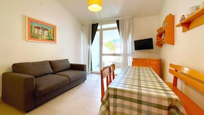 Una habitación con un sofá, una mesa con mantel a cuadros, una televisión y una ventana con cortinas.