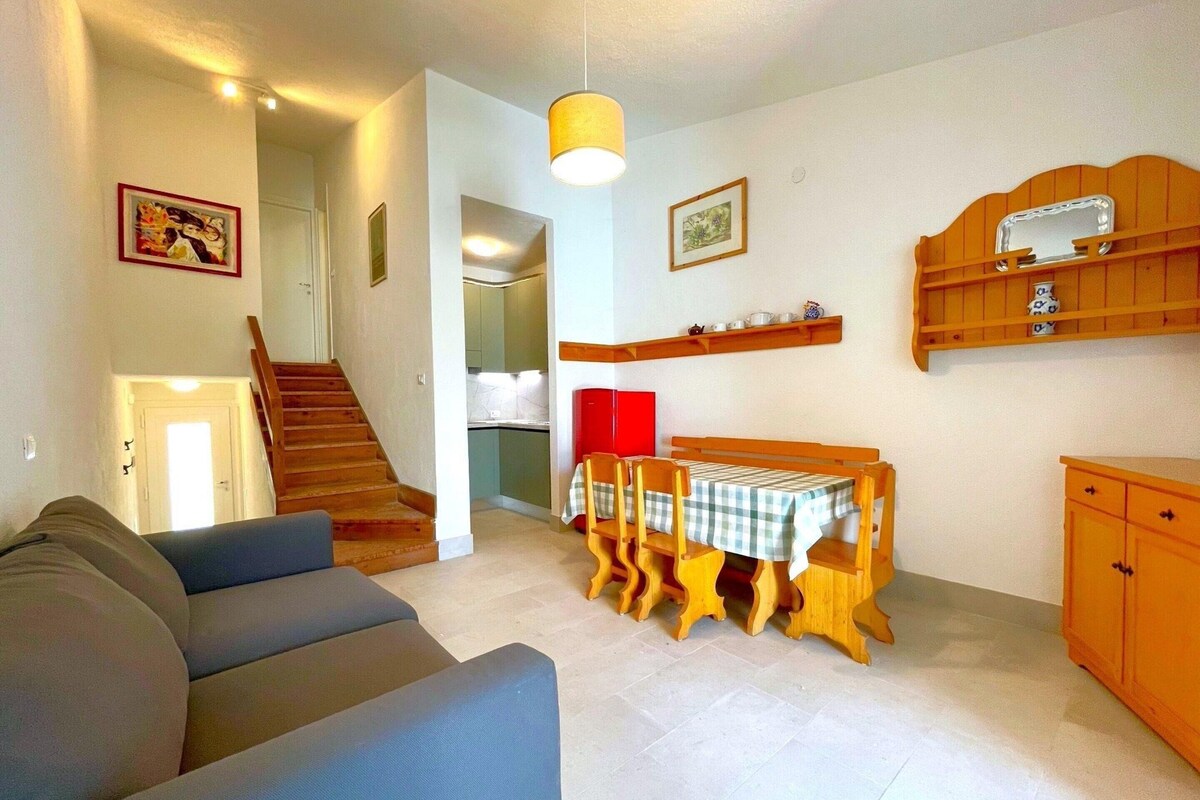 Ein Wohnzimmer mit einer Couch, einem Esstisch mit Stühlen, einer Küchenzeile und einer Treppe.