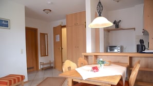 A dining area with a wooden table, chairs, a small rug, a hanging light fixture, and a kitchen area with a microwave and toaster. - Beautiful Lodging in the Alps Near Bayrischzell (Bayrischzell)