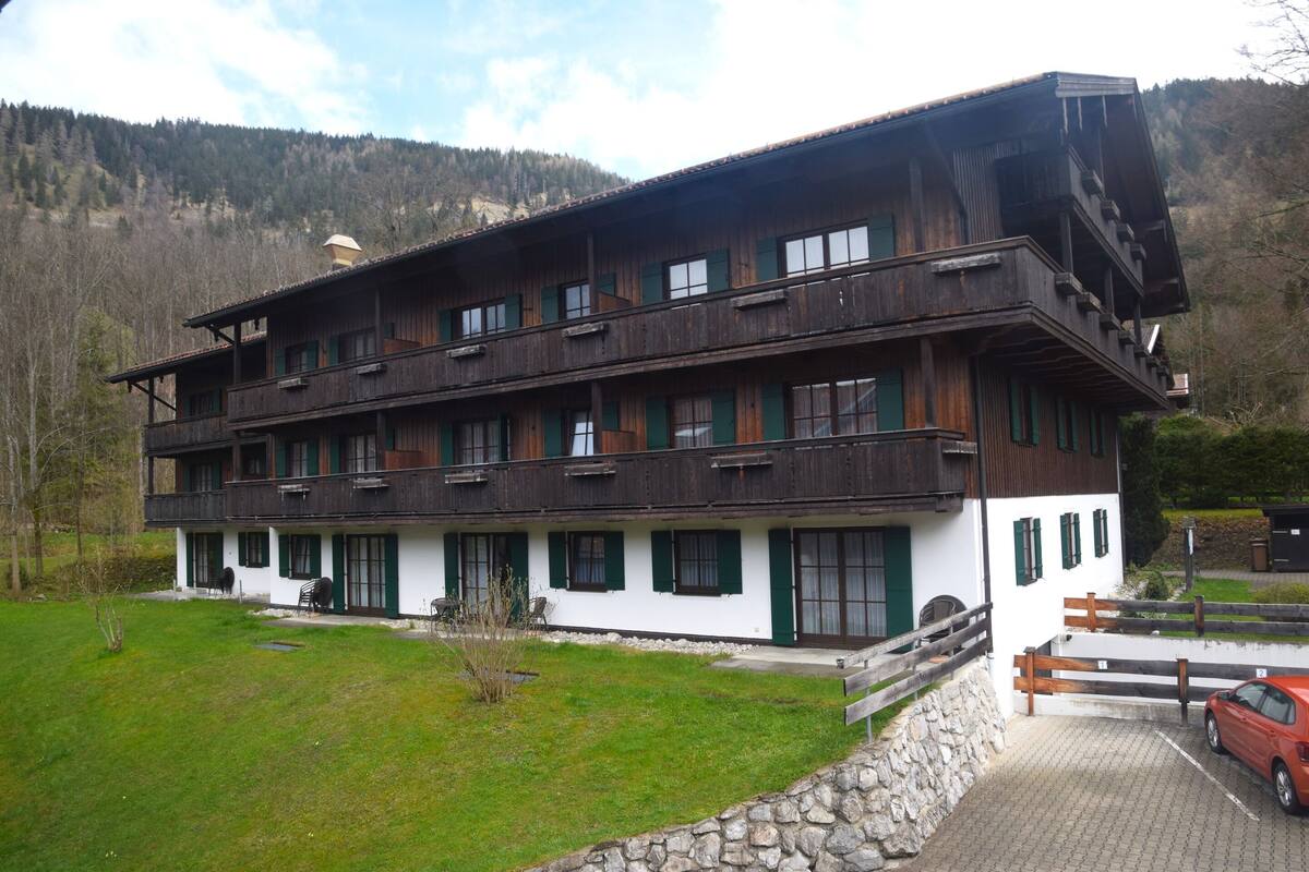 Un immeuble en bois à plusieurs étages, doté de balcons, d’un mur en pierre et d’un espace de stationnement.