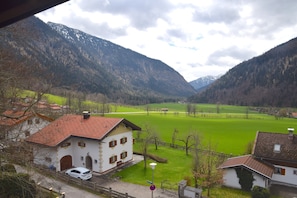 Una casa rural con techo de tejas rojas, fachada blanca y un campo verde al fondo.