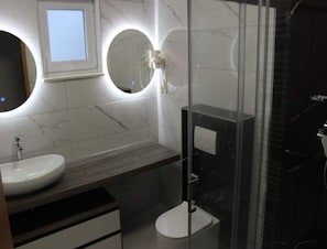 Un baño moderno con tocador de mármol, cabina de ducha con mampara de vidrio y un inodoro.