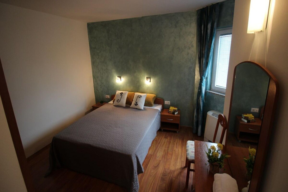 Een slaapkamer met een bed, nachtkastjes, een spiegel, een stoel en een raam met gordijnen.