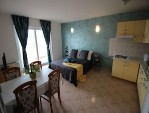 Un espacio habitable compacto con cama, una mesa de comedor con sillas, una kitchenette y una ventana con cortinas.