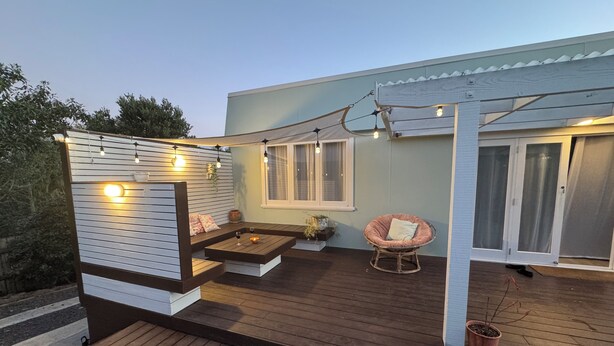A wooden deck with a seating area, string lights, and a potted plant. - Central & Cozy Raglan house - 10min walk to town! (Raglan)