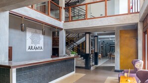 A reception desk with a sign reading 'ARAMYA,' a staircase, and a seating area with a table and chairs. - Aramya Riverfront Boutique Resort (Kitulgala)