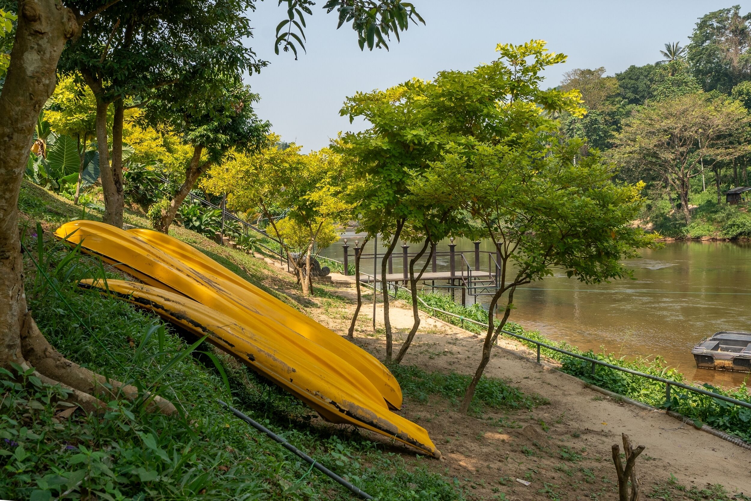 A riverbank with a yellow canoe, trees, and a dock.