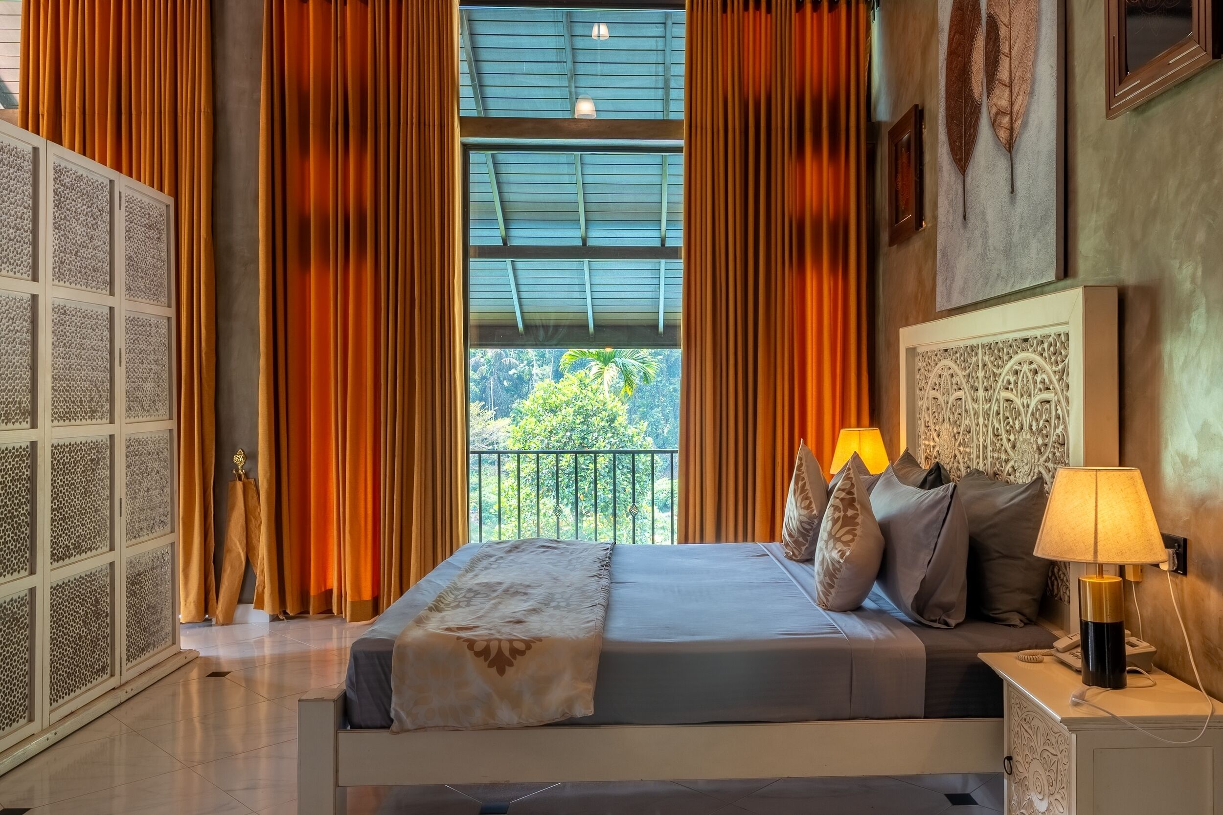 Une chambre à coucher avec un lit, des rideaux, une table de chevet, une lampe et une vue sur la verdure à l’extérieur.