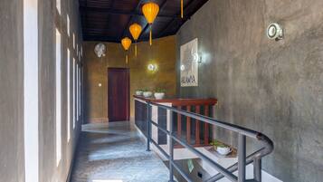 A hallway with a marble floor, a wooden door at the end, a railing with potted plants, and a wall-mounted sign.
