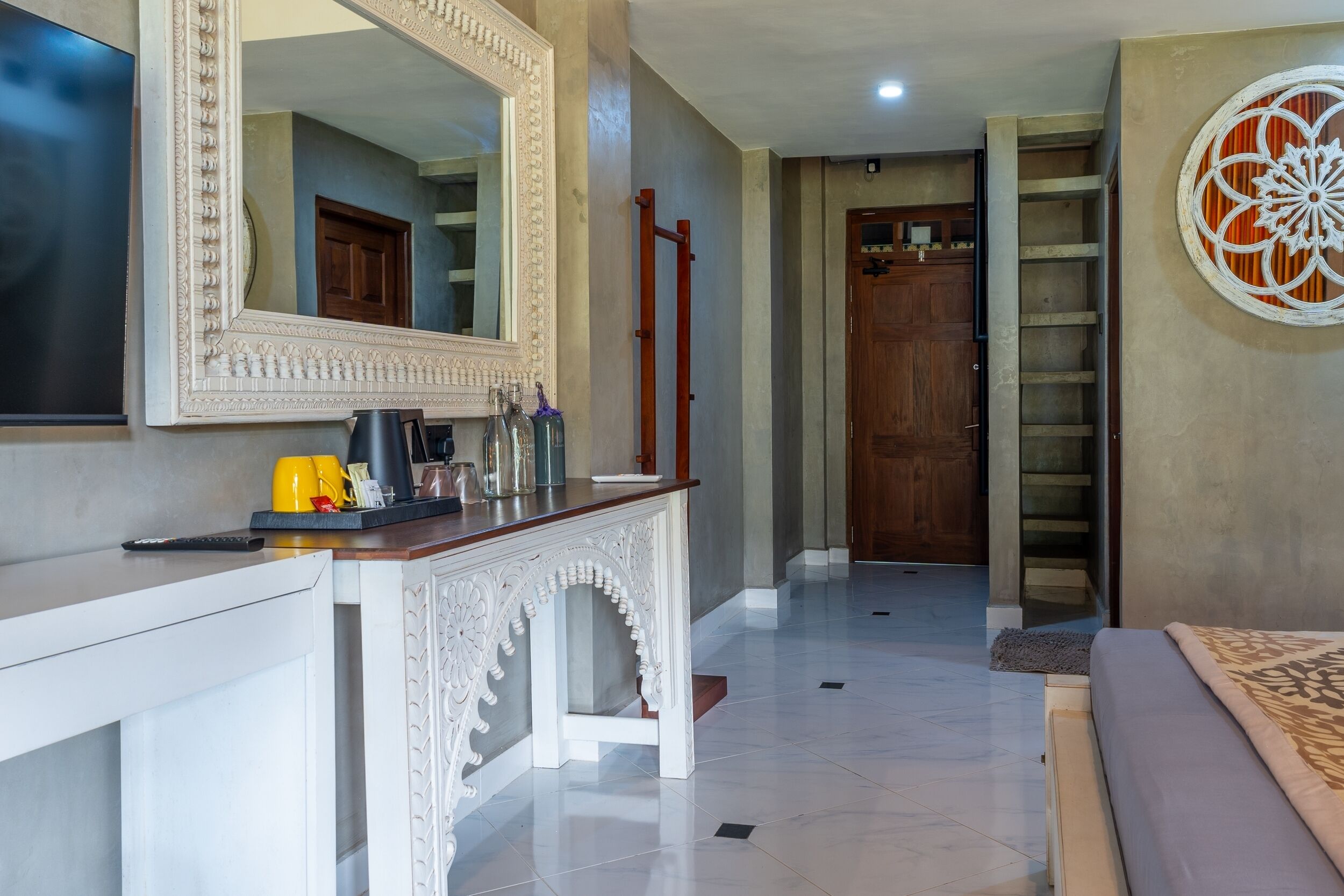 A hotel lobby with a white console table, a large mirror, a wooden door, and a decorative wall piece.