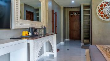 A hotel lobby with a white console table, a large mirror, a wooden door, and a decorative wall piece.