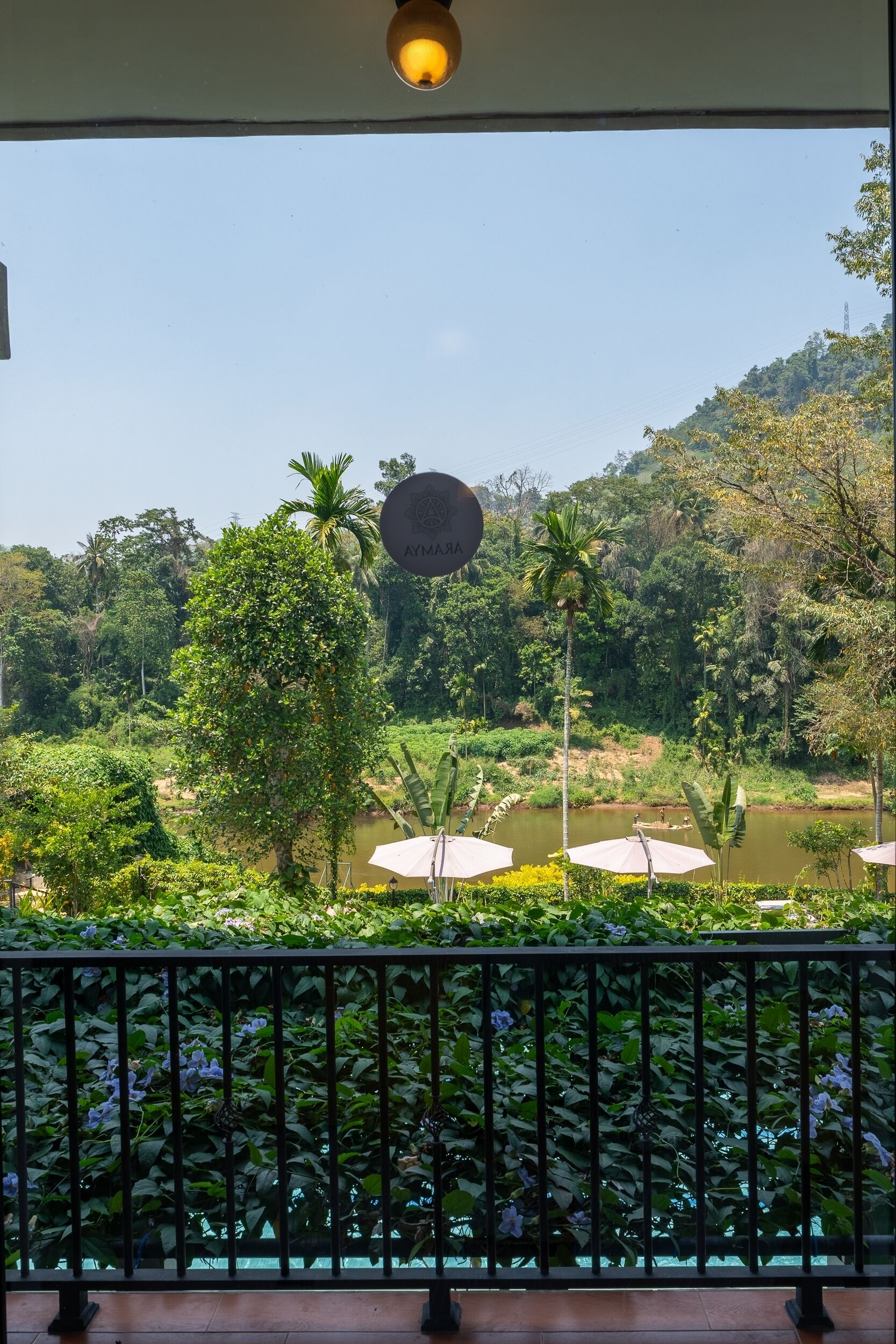 Une vue depuis un balcon doté d’une balustrade, donnant sur une rivière, des arbres et une colline.