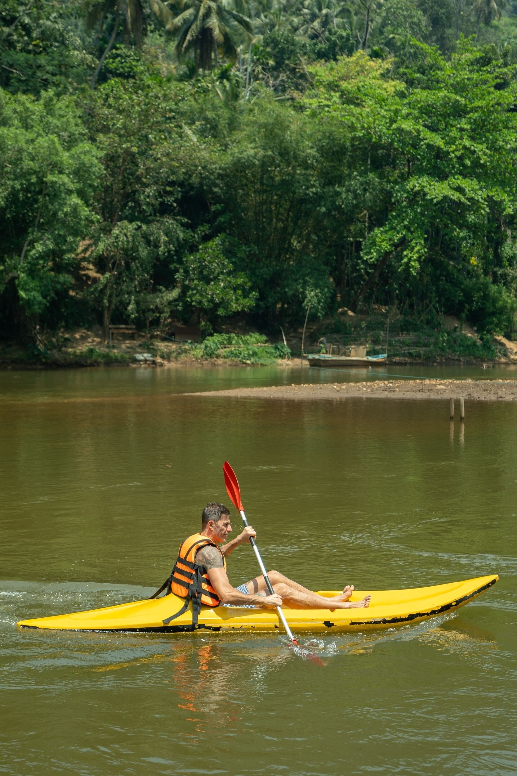 A person kayaking on a river surrounded by dense greenery.