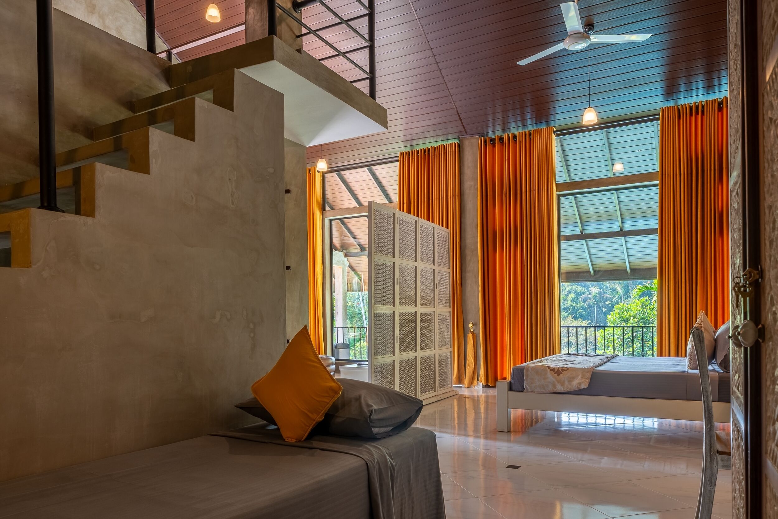 A modern hotel room with a bed, a sofa, a staircase, and large windows with curtains.