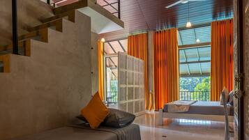 A modern hotel room with a bed, a sofa, a staircase, and large windows with curtains.