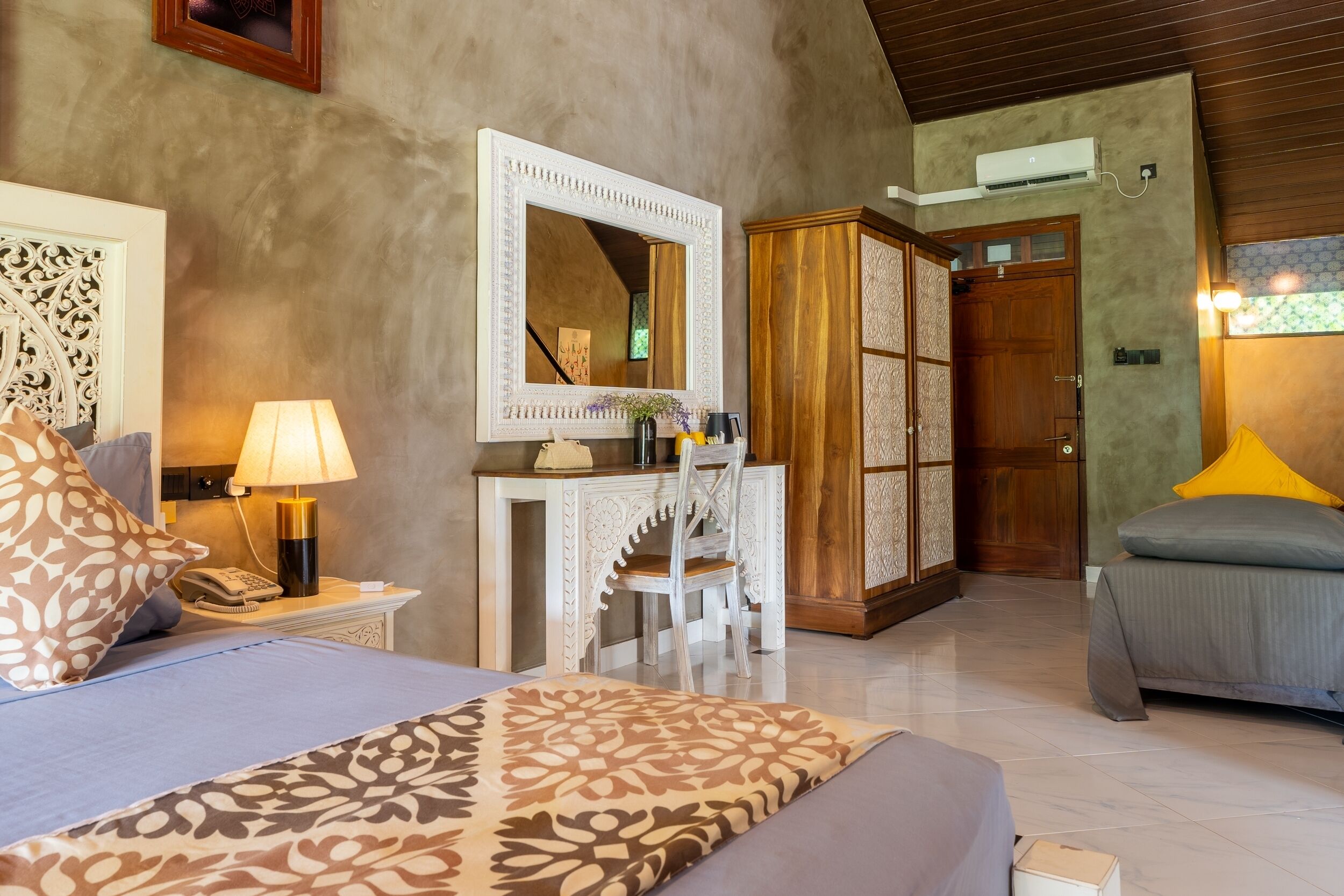 A bedroom with a bed, a desk, a chair, a mirror, a wardrobe, and a nightstand with a lamp.