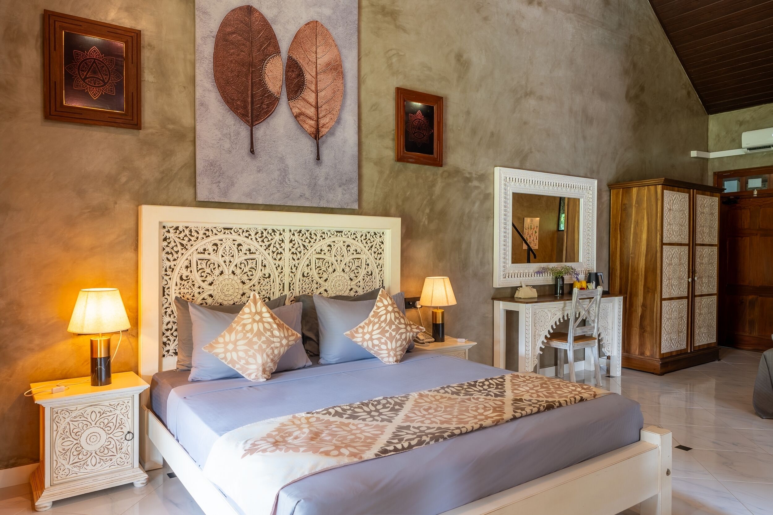A bedroom with a large bed, two bedside tables with lamps, a decorative headboard, and a wardrobe.