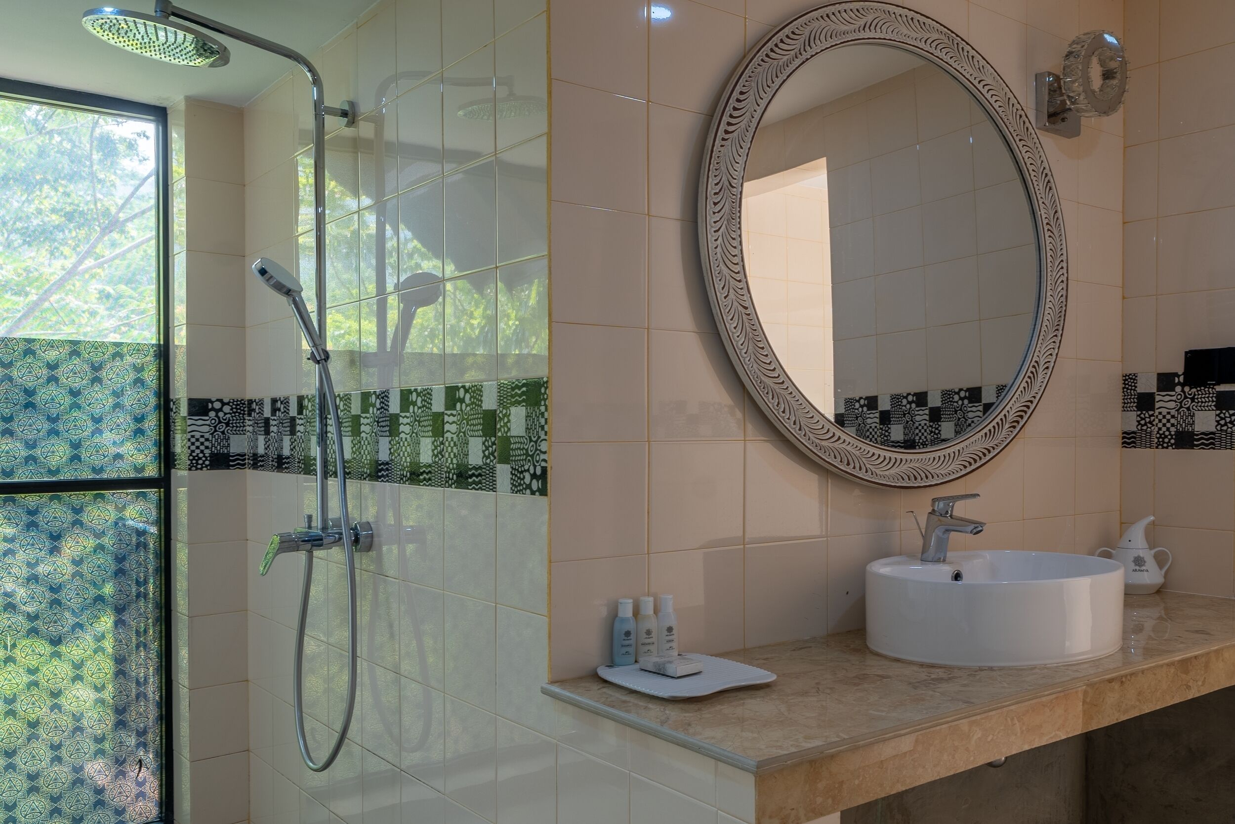 A bathroom with a shower, a sink, a mirror, and patterned tiles.