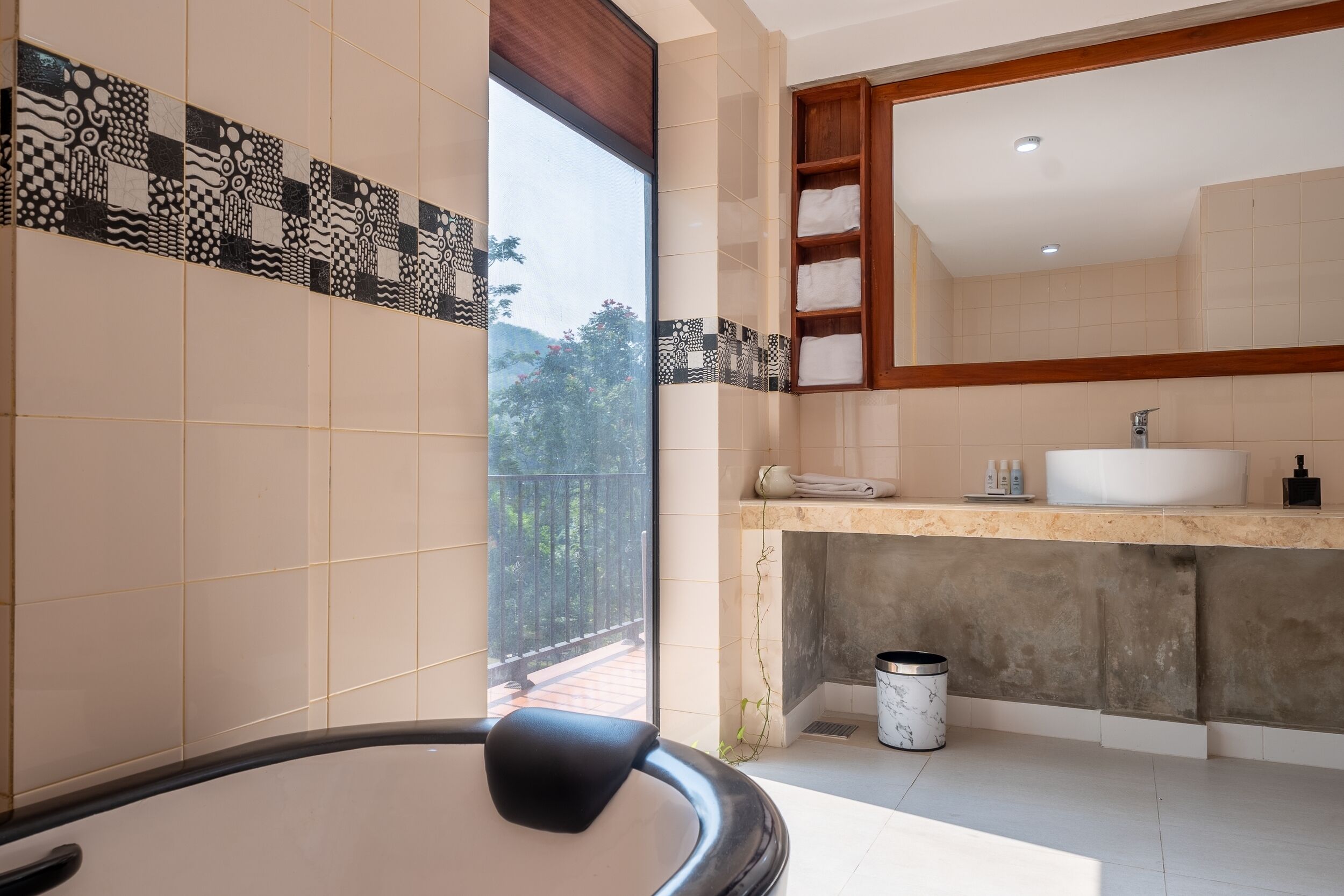A bathroom with a large bathtub, a vanity with a sink, a mirror, and a window with a view of greenery.