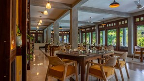 A spacious dining area with wooden tables and chairs, large windows, and ceiling fans. - Aramya Riverfront Boutique Resort (Kitulgala)