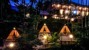 A multi-story building with a well-lit entrance and a series of tents in the foreground. - Aramya Riverfront Boutique Resort (Kitulgala)