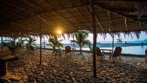 Un espace aménagé au bord de la plage, doté d’un toit de chaume, de chaises longues et offrant une vue sur la mer.