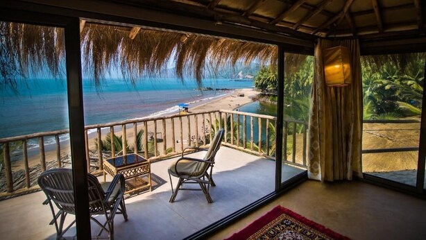 Un balcon avec vue sur la plage et l’océan, deux fauteuils en osier, une petite table et un tapis rouge.