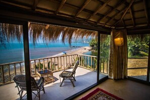 A balcony with a view of the beach and ocean, two wicker chairs, a small table, and a red rug. - Dwarka Beach Resort Goa (Canacona)